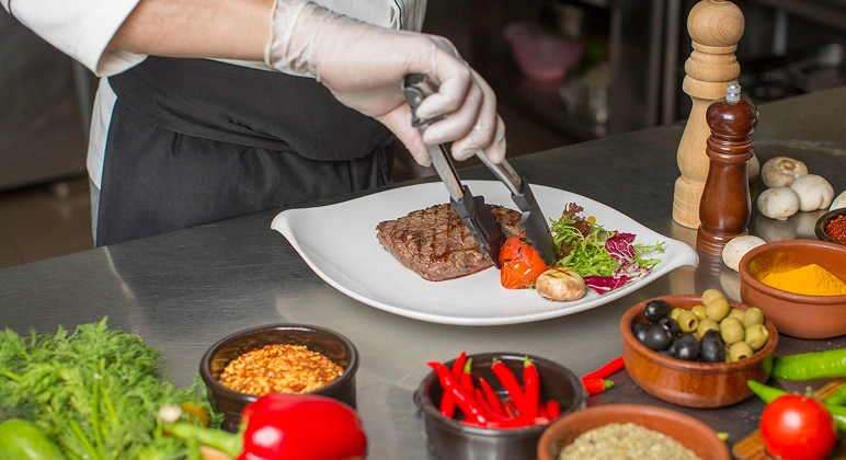 Chef plating grilled steak with vegetables