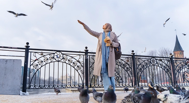 Muslim woman feeding pigeons on waterfront bridge